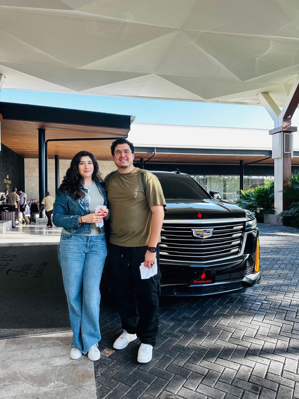 Pareja junto a una Cadillac Escalade negra a la entrada de un resort